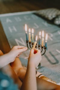 A child lighting a menorah with candles during a cozy indoor Hanukkah celebration.